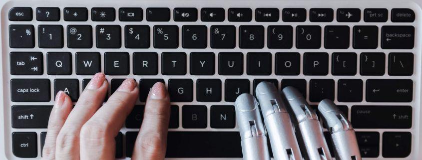 creare-contenuti-con-l-intelligenza-artificiale-opportunita-e-rischi Una mano robotica e una mano umana sulla tastiera