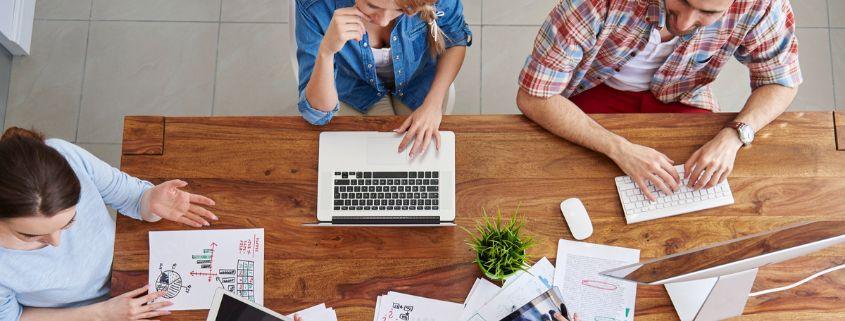 Team di lavoro impegnato a un tavolo con computer portatili e documenti